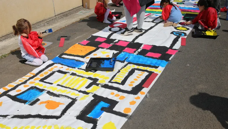 Enfants peignant de grands motifs colorés sur une bande de papier au sol